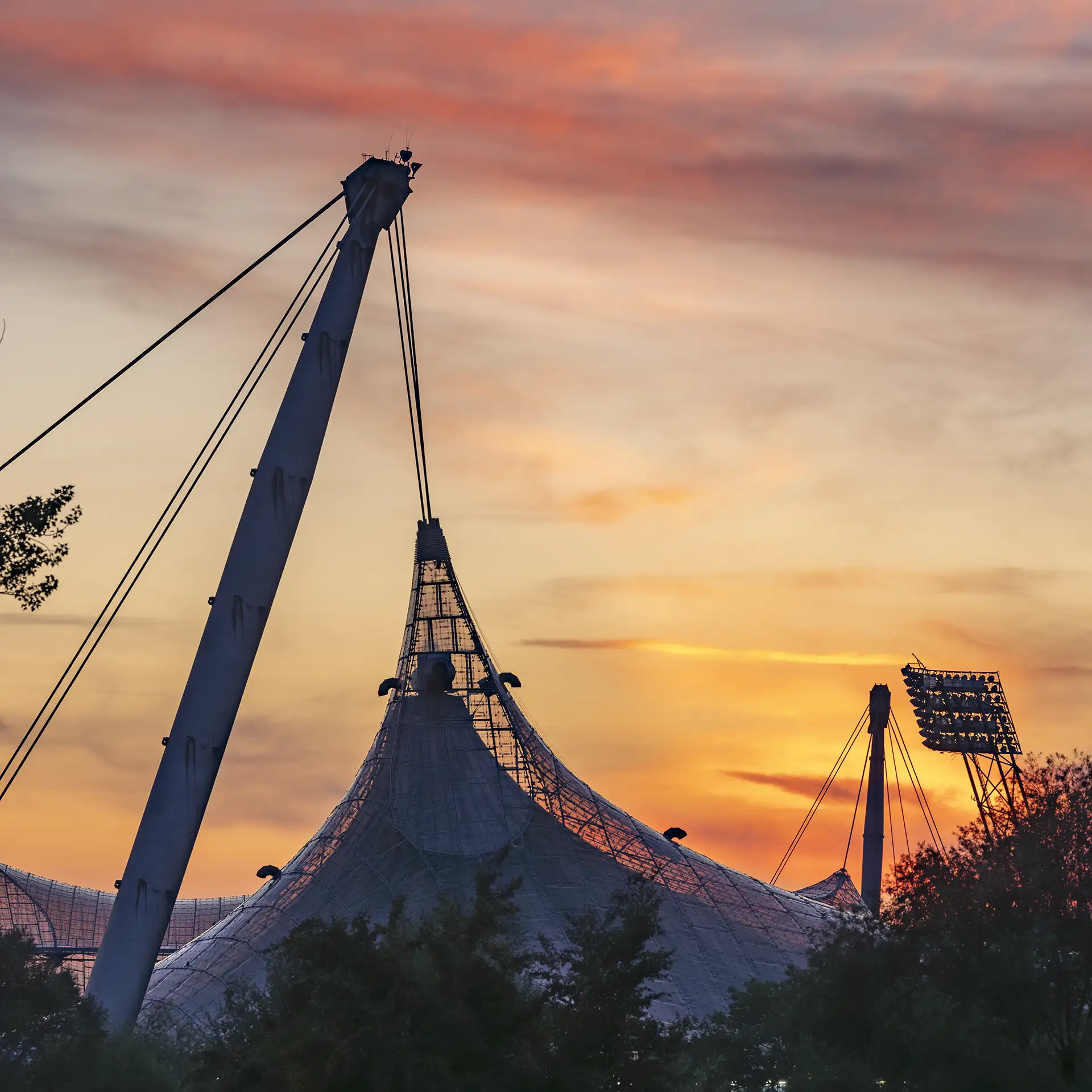 Farbfoto: Verdichteter Blick auf Teile des Münchner Olympiadaches, dramatisch gelbroter Himmel der untergehenden Sonne im Hintergrund
