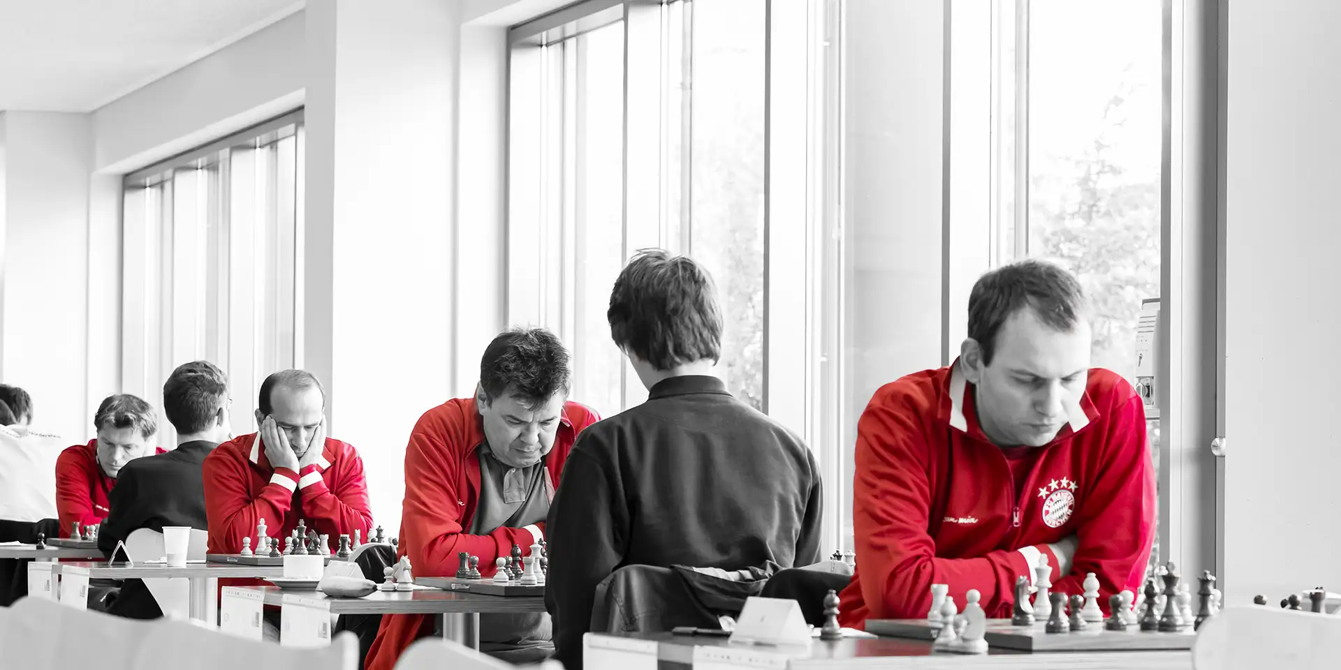 4 Schachspieler des FC Bayern München in roten Trikots im Spiel mit ihren GHegnern vor einer hellen Fensterwand